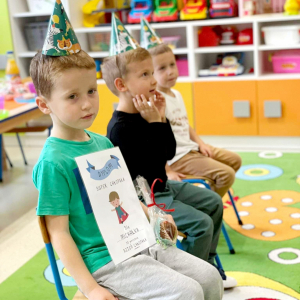 Urodziny kolegów z grupy Biedronki, trzech chłopców w urodzinowej czapce siedzą na krześle w sali przedszkolnej.