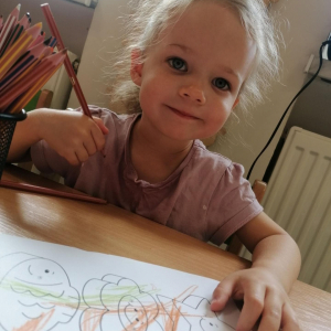 Dziewczynka uśmiecha się podczas kolorowania obrazka