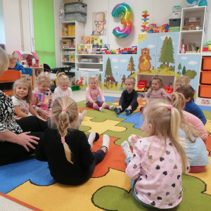 Dzieci siedzą na dywanie z pedagogiem
