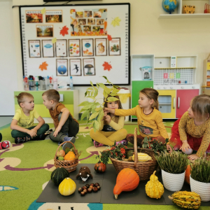 Dzieci siedzą na dywanie i poznają dary jesieni