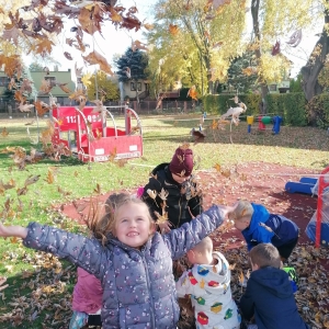 Na zdjęciu dzieci z grupy Sówki bawią się jesiennymi liśćmi przy przedszkolu