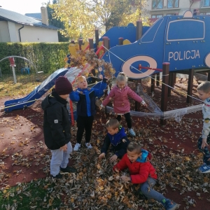 Na zdjęciu dzieci z grupy Sówki bawią się jesiennymi liśćmi przy przedszkolu