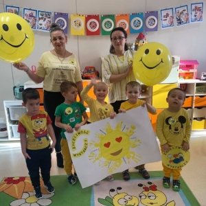 Na zdjęciu widać dzieci z grupy Myszki wraz z Panią Marzeną i Panią Jadzią. Wszyscy są ubrani w żółte bluzki i prezentują plakat z okazji Dnia życzliwości