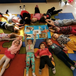 Dzieci leżą na dywanie w sali przedszkolnej