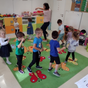 Dzieci tańczą w swojej sali w kole. Dzieci naśladują nauczyciela.
