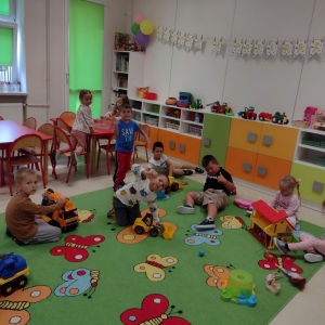 Dzieci bawią się na dywanie w sali przedszkolnej.