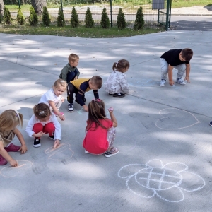 Dzieci bawią się na placu zabaw przy przedszkolu. Rysują kredą na betonie.