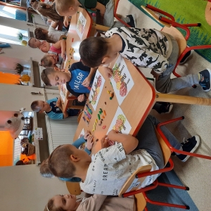 Dzieci siedzą przy stolikach w swojej sali. Wyklejają pracę kropkami z plasteliny.