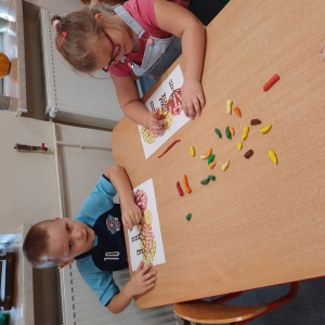 Dzieci siedzą przy stolikach w swojej sali. Wyklejają pracę kropkami z plasteliny.