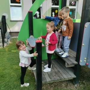 Dzieci bawią się na placu zabaw przy przedszkolu. Dzieci są radosne.
