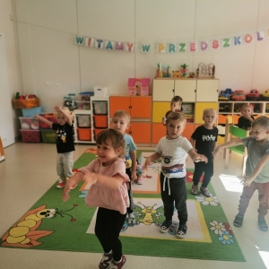 Na zdjęciu dzieci tańczą w sali przedszkolnej. Śmieją się.